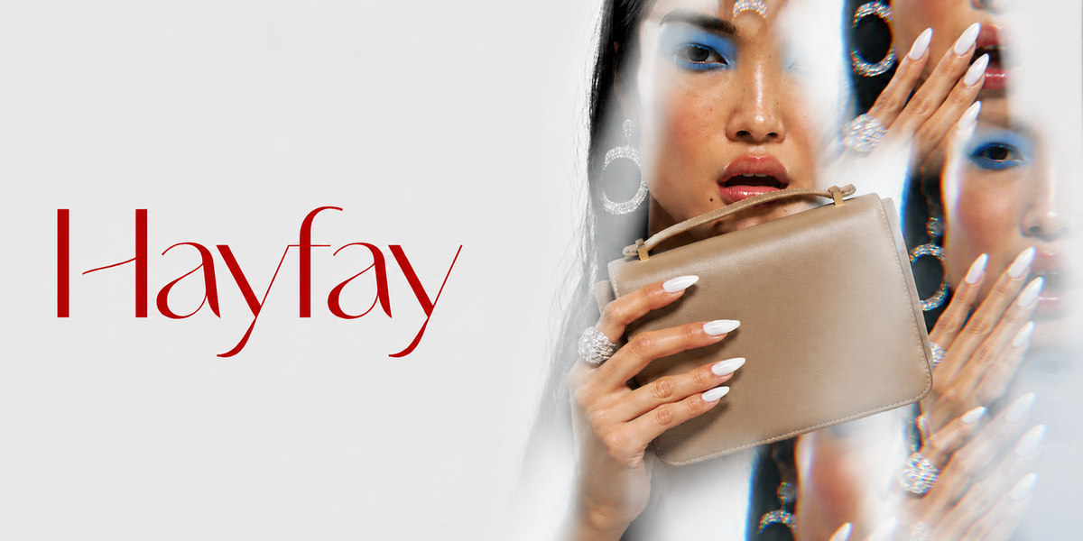 A beige leather handbag held by a model with dramatic blue eye makeup and white manicured nails, with the brand name 'Hayfay' written in red script on the left against a light gray background.